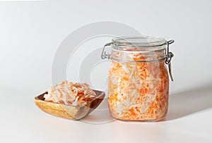 Homemade sauerkraut. Fermented food. Sauerkraut with carrots in a glass jar and a wooden bowl on a white background