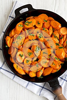 Homemade Sauteed Carrots in a cast iron pan on a white wooden surface, top view. Flat lay, overhead, from above. Close-up