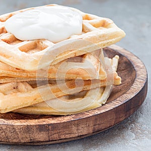 Homemade savory belgian waffles with bacon and shredded cheese, served with plain yogurt on a wooden plate, square