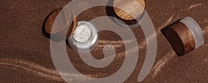 Homemade scrub with brown sugar and coffee in glass jar with wooden lid on brown sand background.