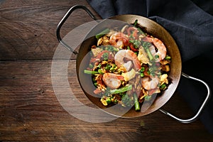 Homemade seafood dish with rice, prawns, chicken and vegetables in a Spanish paella pan on a dark rustic wooden table, copy space