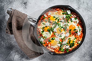 Homemade shakshuka, fried eggs, onion, bell pepper, tomatoes and parsley in a pan. Gray background. Top view