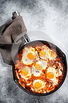 Homemade shakshuka, fried eggs, onion, bell pepper, tomatoes and parsley in a pan. Gray background. Top view