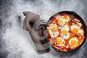 Homemade shakshuka, fried eggs, onion, bell pepper, tomatoes and parsley in a pan. Gray background. Top view. Copy space