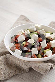 Homemade Shepards salad with cucumbers, parsley and feta in a white bowl on a white wooden surface, side view. Closeup photo