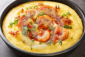 Homemade shrimp and grits with smoked bacon, onions and cheese in a black bowl on a dark concrete background. Horizontal