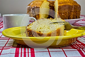 Homemade simple cake. Detail of homemade cake slice being cut with fork on a yellow plate with cup of coffee and cake in the backg