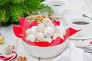Homemade snowballs cookies with walnuts in icing sugar in a bowl on a white wooden background.