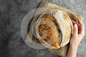 Homemade sourdough bread, female hands holding rustic round loaf, top view