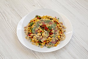 Homemade southwestern egg scramble on a white plate on a white wooden background, side view