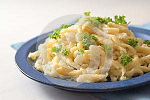 Homemade spaetzle with parsley garnish on a blue plate and a white table, typical dish in Schwaben, southern Germany and Austria,