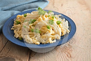 Homemade spaetzle served with parsley garnish on a blue plate and a rustic wooden table, traditional egg pasta in Schwaben,