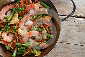 Homemade Spanish Paella, rice dish with seafood, chicken and vegetables in a pan on a rustic wooden table, close up, high angel