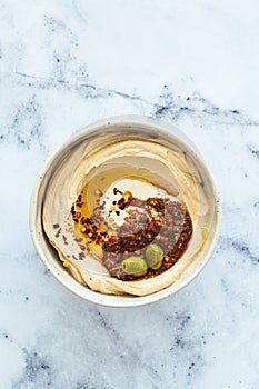 Homemade spicy hummus with tahini and olive oil in bowl, white marble background. Israeli traditional food