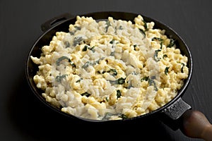 Homemade Spinach Mac and Cheese in a cast-iron pan on a black background, side view. Close-up