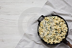 Homemade Spinach Mac and Cheese in a cast-iron pan on a white wooden background, top view. Flat lay, overhead, from above. Copy