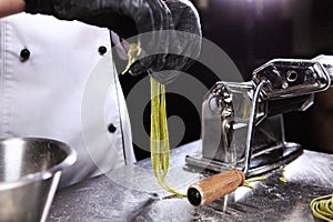 Homemade spinach pasta in the hands of the chef. Photo on a black background. Unrecognizable person. CMachine for making pasta at