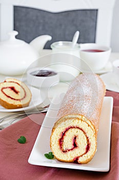 Homemade sponge cake with raspberry jam on a white plate on a white wooden dining table.