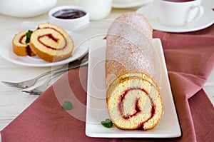 Homemade sponge cake with raspberry jam on a white plate on a white wooden dining table.