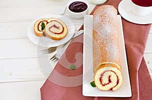 Homemade sponge cake with raspberry jam on a white plate on a white wooden dining table.