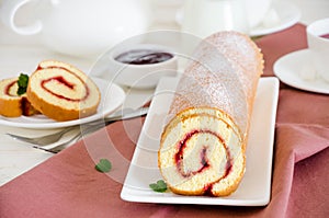 Homemade sponge cake with raspberry jam on a white plate on a white wooden dining table.