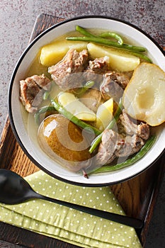 Homemade stew made from lamb meat, fresh pears, potatoes, green beans close-up in a bowl on a wooden board. Vertical top view