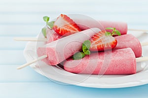 Homemade strawberry ice cream or popsicles in plate on blue wooden table, frozen fruit juice