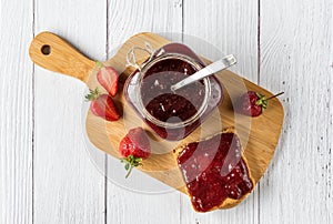 Homemade strawberry jam in a glass jar and spread over toast bread