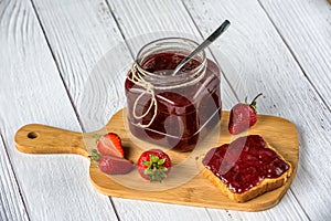 Homemade strawberry jam in a glass jar and spread over toast bread