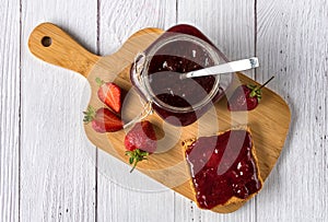 Homemade strawberry jam in a glass jar and spread over toast bread