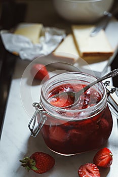 Homemade strawberry jam in a jar, fresh strawberries, bread and butter on kitchen table