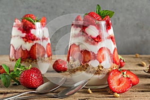 Homemade strawberry yogurt parfait with granola, mint and fresh berries in glasses on rustic wooden table