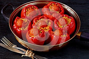 Homemade stuffed red bell peppers with rice and vegetables in a vintage frying pan on the black background