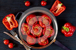 Homemade stuffed red bell peppers with rice in a vintage frying pan decorated with fresh cherry tomatoes on the black background