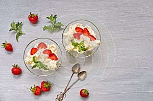 Homemade summer dessert with sliced strawberries and cream cheese in the glass bowls on a gray background with copy space