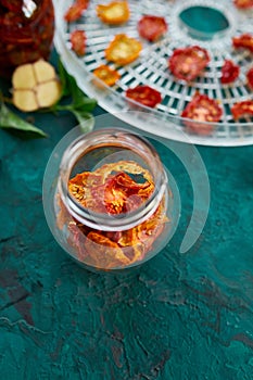 Homemade sun dried tomatoes with herbs, garlic in olive oil in a glass jar on dark green background. Copy space, close up.