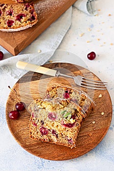 Homemade sweet cherry loaf cake with nuts on wooden plate. Light blue concrete background. Selective focus