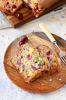 Homemade sweet cherry loaf cake with nuts on wooden plate. Light blue concrete background. Selective focus