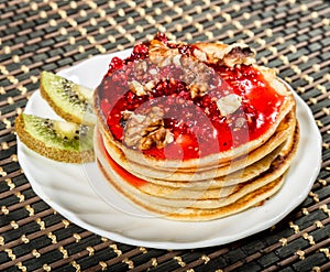 Homemade sweet pancakes with raspberry jam on a white plate. Breakfast with stack topped blueberry jam, walnuts and kiwi