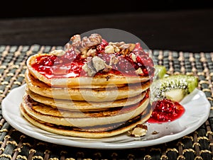 Homemade sweet pancakes with raspberry jam on a white plate. Breakfast with stack topped blueberry jam, walnuts and kiwi