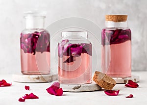 Homemade sweet rose water or syrup in glass bottles with pink petals in it. Healthy summer food concept.