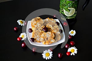 Homemade sweetness of toffee, butter and corn sticks on a white square plate, decorated with daisies with ladybirds and cherries