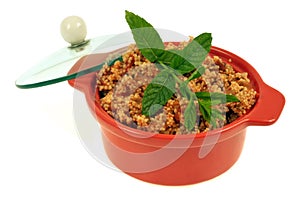 Homemade tabouleh served in a ramekin with mint leaves in closeup on white background