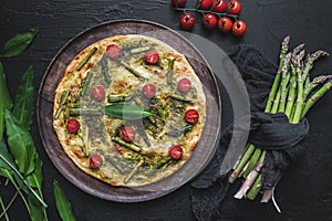 Homemade tarte flambee with green asparagus, tomatoes and wild garlic pesto on a wooden plate