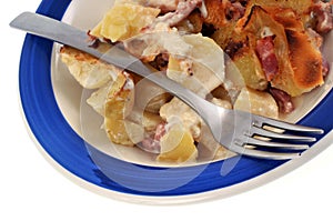 Homemade tartiflette served in a plate with a fork close-up on a white background