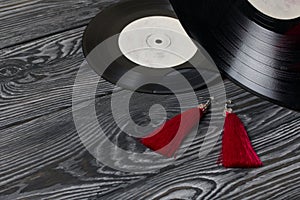 Homemade tassel earrings in red. Against the background of old vinyl records and brushed pine boards painted in black and white