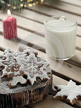 Homemade tasty christmas gingerbread cookies with glass of milk on brown wooden background. Close-up. Branches of a Christmas tree