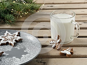 Homemade tasty christmas gingerbread cookies with glass of milk on brown wooden background. Close-up. Branches of a Christmas tree