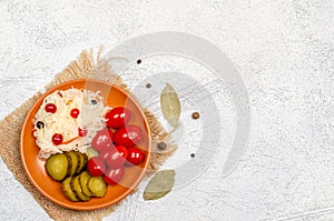 Homemade tasty fermented products on a plate - sauerkraut, tomatoes, pickles, peppercorns, bay leaf on a white background, copy