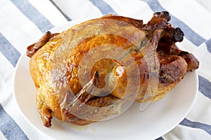 Homemade tasty rotisserie chicken on white plate, side view. Close-up